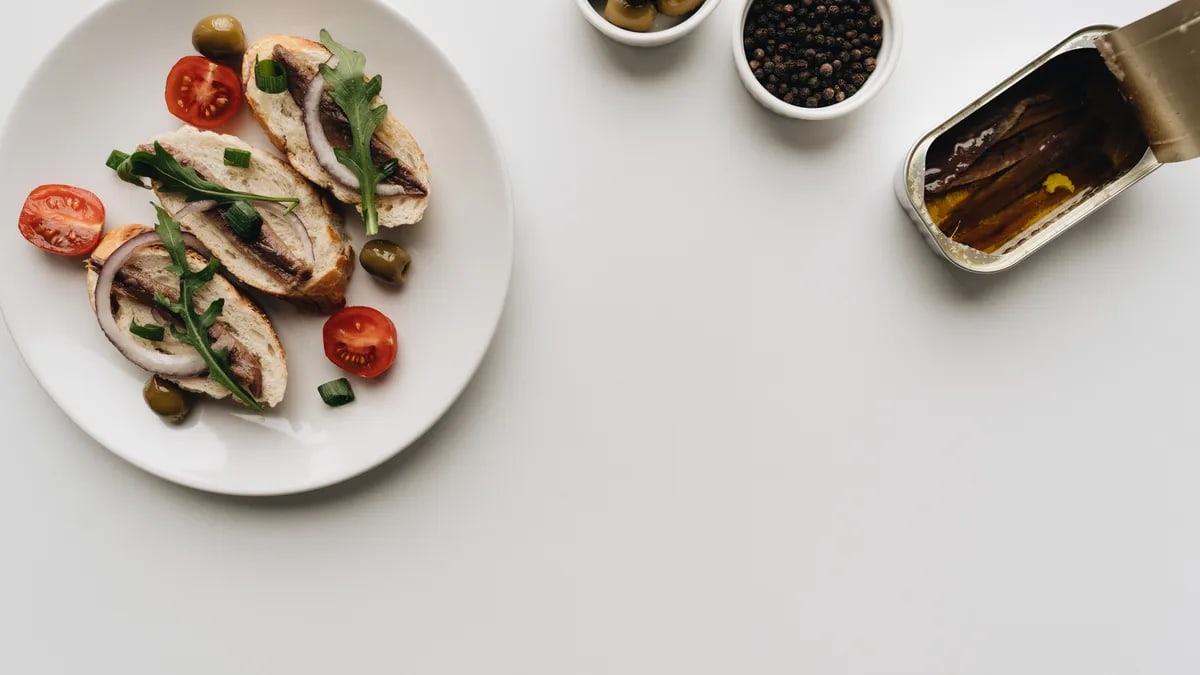 Top view of delicious Mediterranean dish with anchovies, olives, and tomatoes on white background.